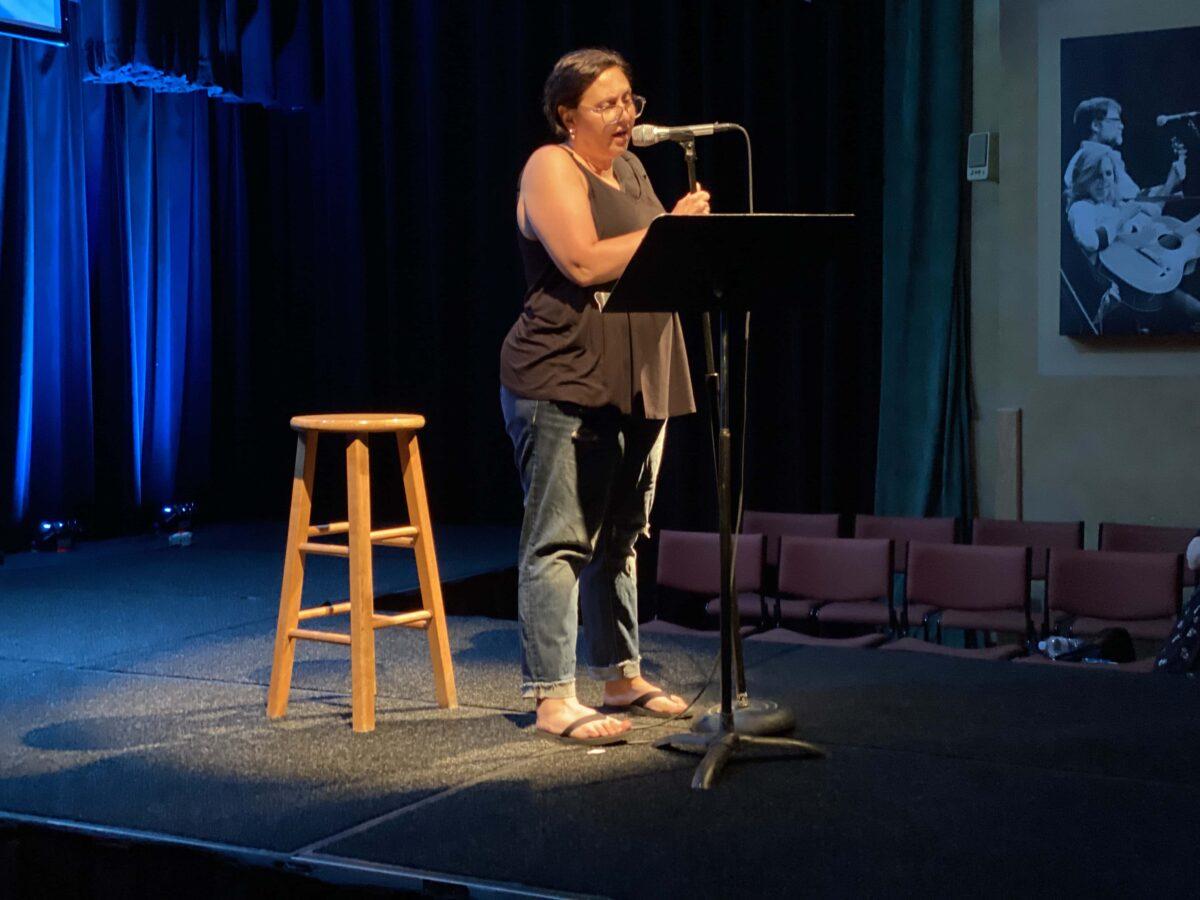 Photo of Mary Panza on stage at The Linda talking into a microphone