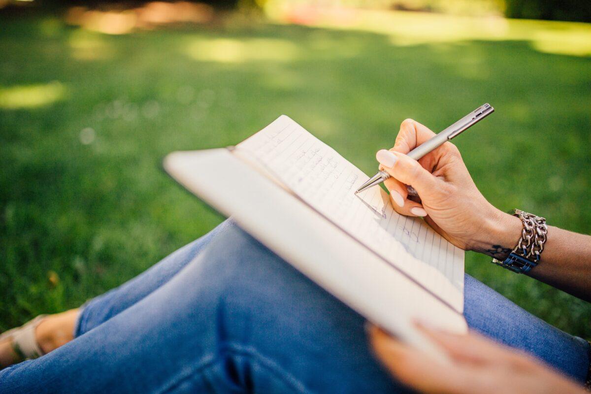 Writing in a notebook sitting in the grass