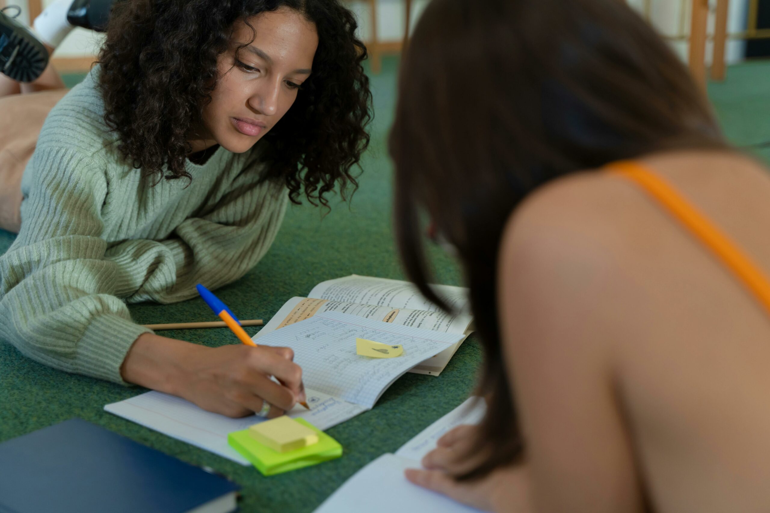 A Girl Wearing Sweater Writing on a Notebook on the Floor